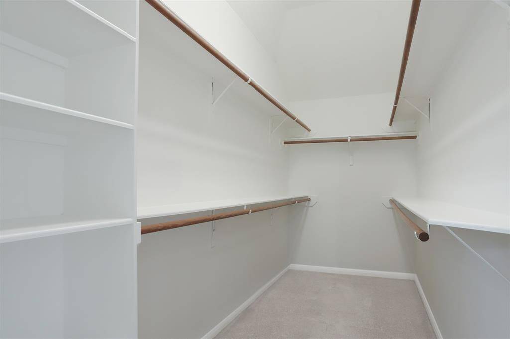 This photo shows a spacious walk-in closet with multiple wooden hanging rods and white shelving, offering ample storage and organization options.