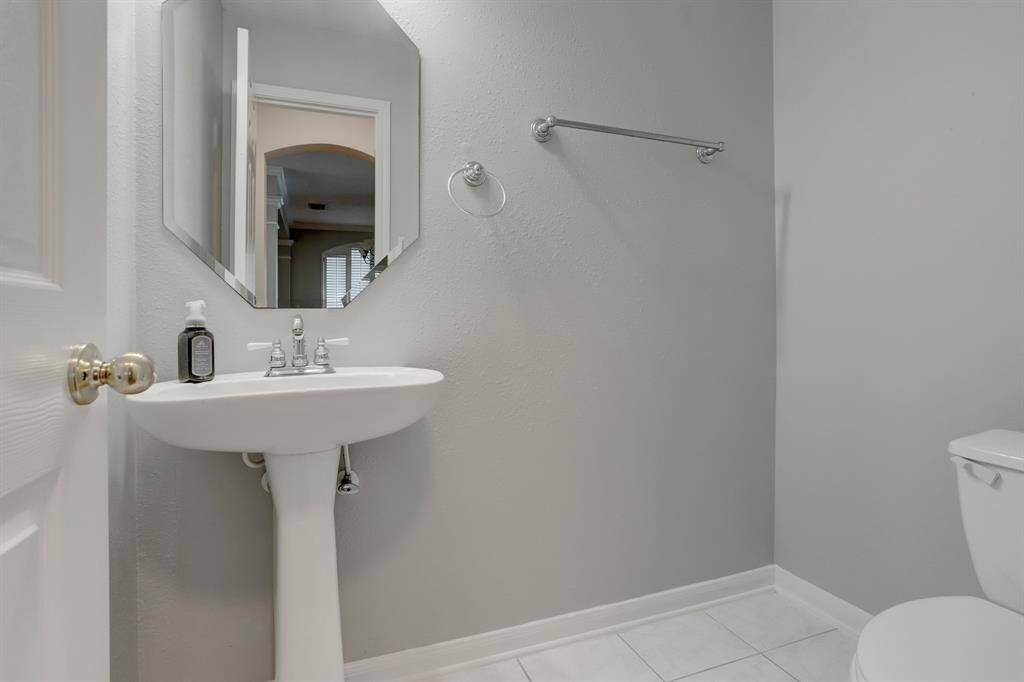 This is a clean, modern half-bathroom featuring a pedestal sink, octagonal mirror, and neutral gray walls. It includes a towel bar and a toilet, with a simple and functional design.
