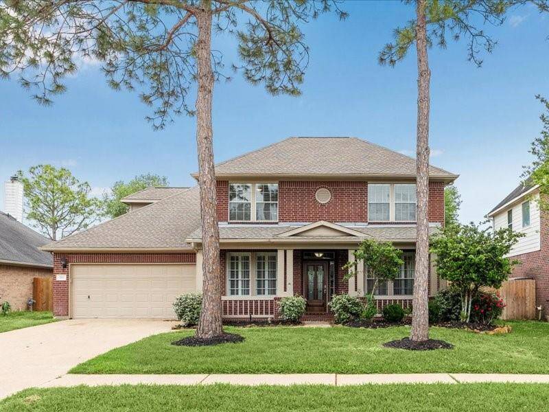 This photo showcases a charming two-story brick home with a welcoming front porch, a well-maintained lawn, and mature trees. The property includes a two-car garage and features a classic, symmetrical design.