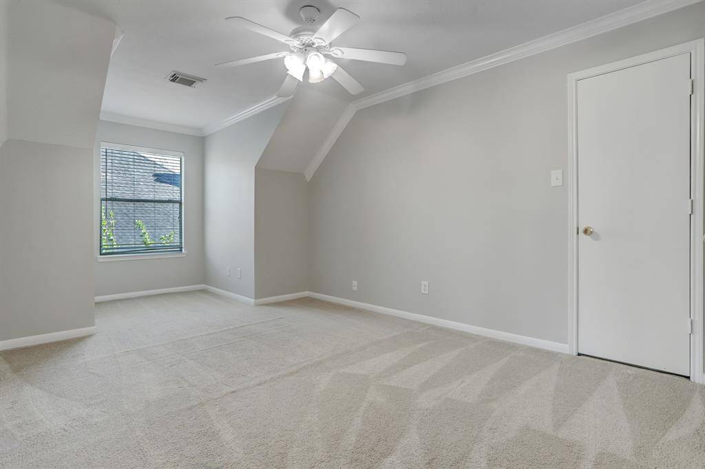 This is a bright, spacious room with neutral-colored walls and carpet. It features a ceiling fan, a window for natural light, and a simple white door. Ideal for a bedroom or office space.