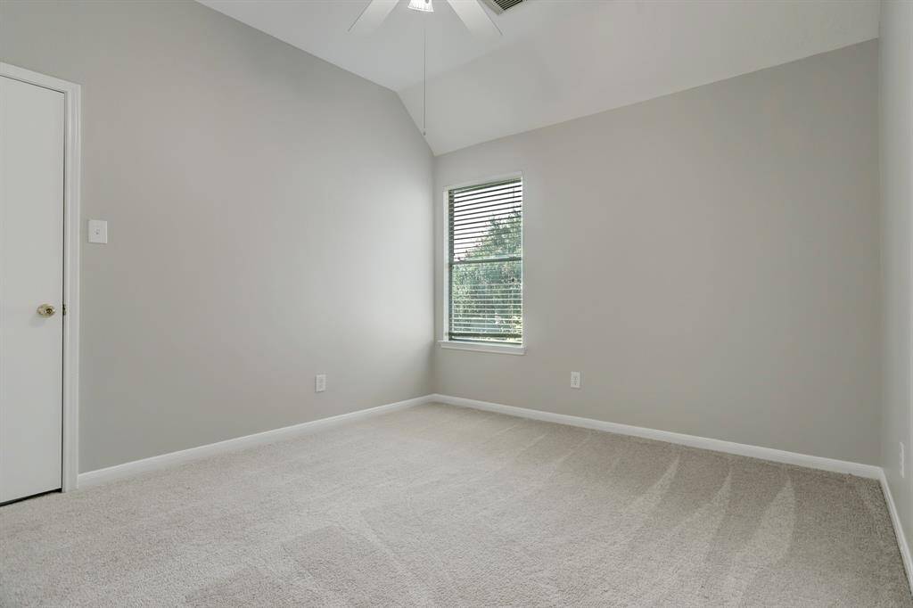 This room features neutral-colored walls, a cozy carpeted floor, and a window with blinds that offers natural light. It includes a ceiling fan for comfort and a simple door, perfect for a bedroom or office space.