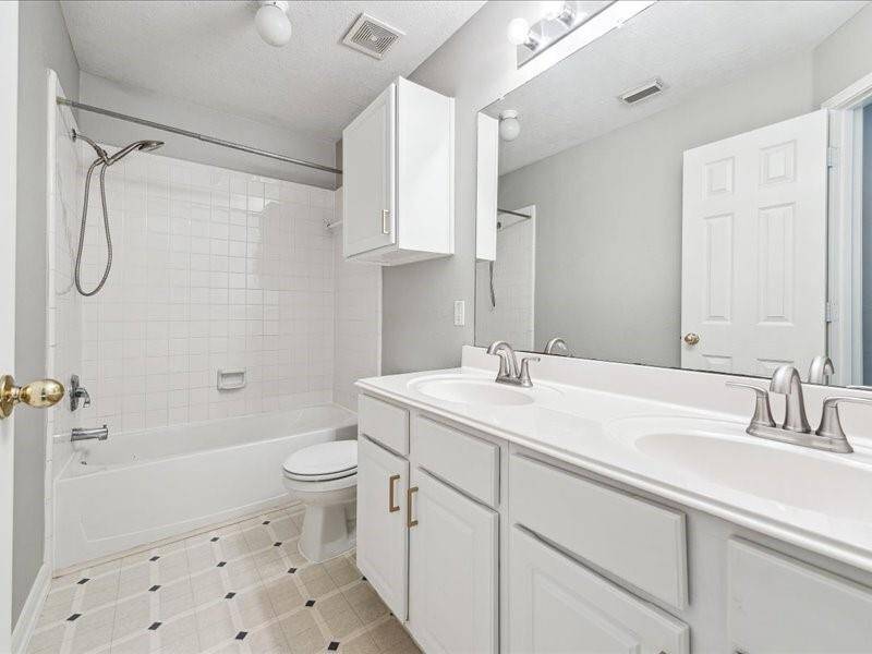 This bright bathroom features a double vanity with ample storage, a full bathtub with a shower, and modern fixtures. The neutral color scheme enhances the space, complemented by a tiled floor.