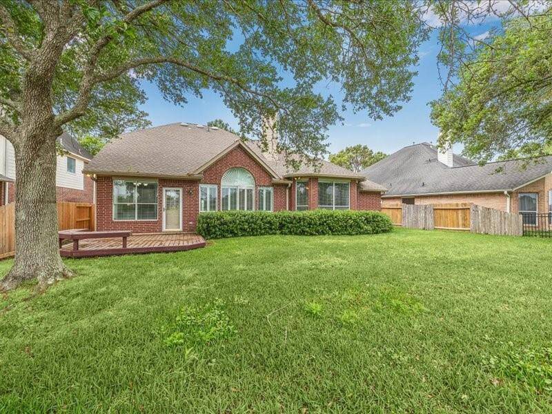 This photo showcases a charming brick house with a well-maintained lawn, a large tree providing shade, and a wooden deck in the backyard, perfect for outdoor activities.