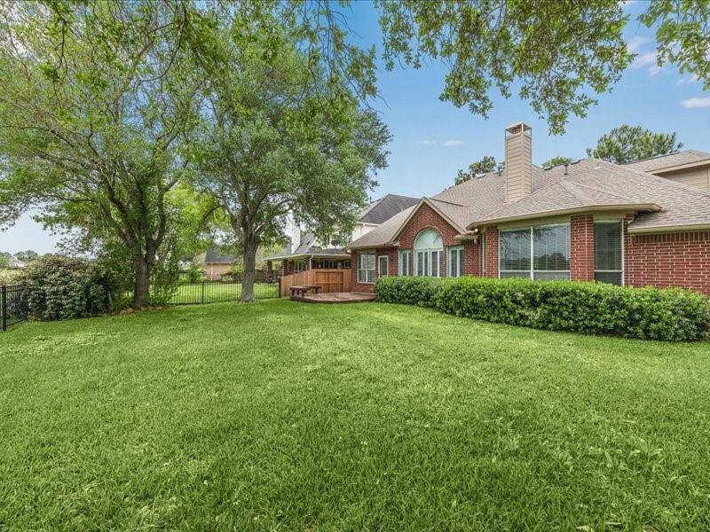 Spacious backyard featuring lush green grass, mature trees, and a charming brick house with large windows and a cozy patio area. Ideal for outdoor relaxation and entertaining.
