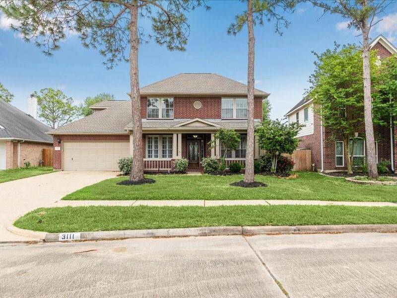 This charming two-story brick home features a welcoming front porch, a well-maintained lawn, and mature trees. It includes a two-car garage and is situated in a quiet suburban neighborhood, offering a peaceful residential atmosphere.