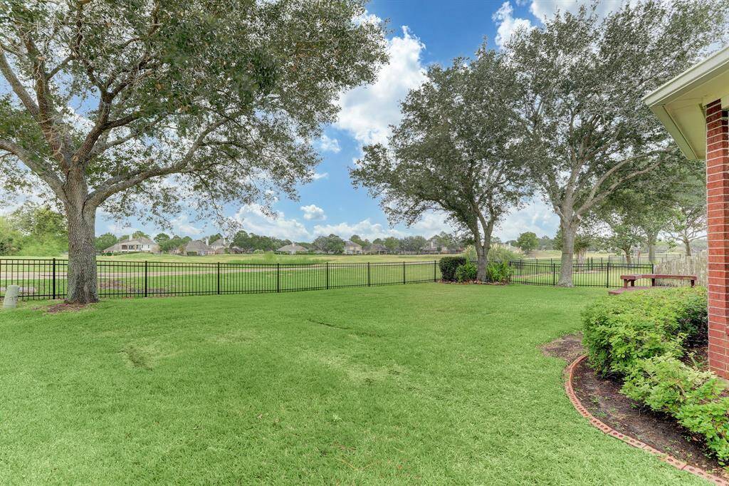 This photo showcases a spacious, well-maintained backyard with lush green grass, mature trees, and a view of a large open field beyond a metal fence. The area provides a sense of privacy and tranquility, ideal for outdoor activities and relaxation.