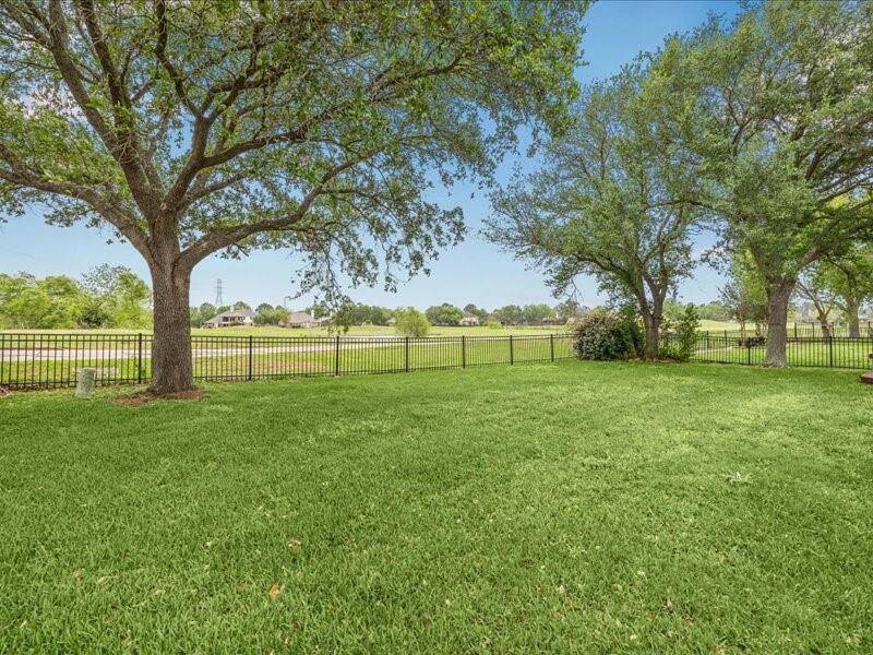 This photo showcases a spacious, well-maintained backyard with lush green grass and mature trees. It features a metal fence providing an open view of a serene landscape beyond, offering a sense of privacy and tranquility. Perfect for outdoor activities and relaxation.