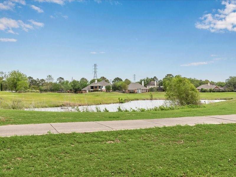 This photo showcases a peaceful residential area with a view of a small pond, surrounded by green lawns and trees. A paved walkway runs along the foreground, offering a serene setting ideal for outdoor activities and relaxation.