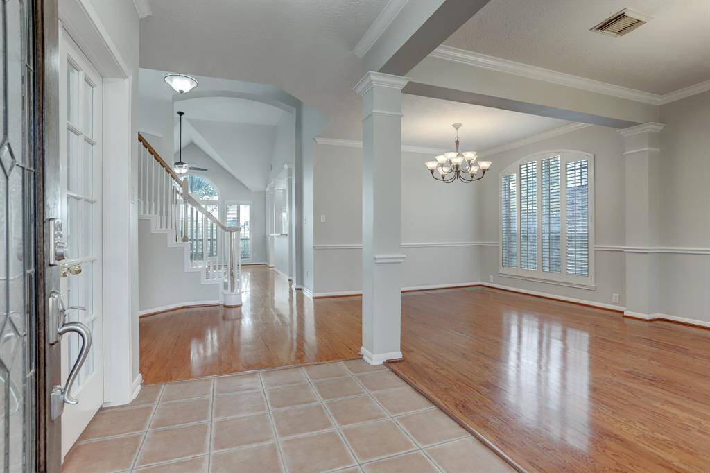 This inviting entryway features elegant tile flooring and transitions to warm hardwood in the adjacent dining area. A beautiful staircase with white railings adds charm, while large windows and a stylish chandelier provide plenty of natural light and sophistication.