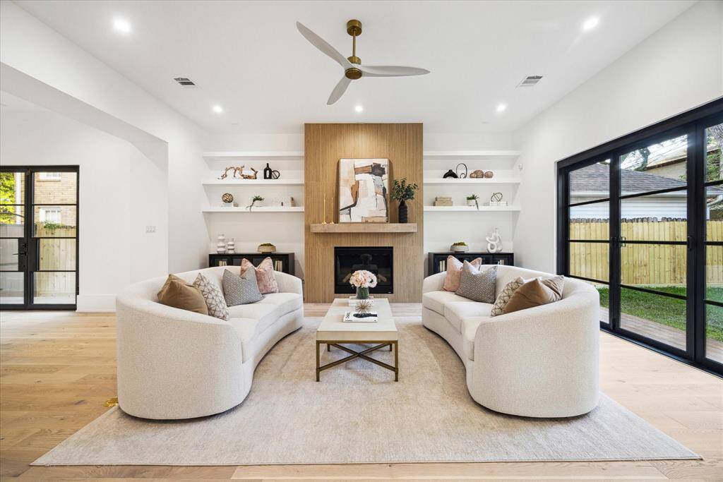 [FAMILY ROOM] The family room is a welcoming and bright retreat, featuring an open and airy layout that invites natural light to fill the space. A striking feature wall with a beautiful fireplace serves as the room's focal point, adding both warmth and modern elegance. Floating shelves along the wall offer stylish storage and display space