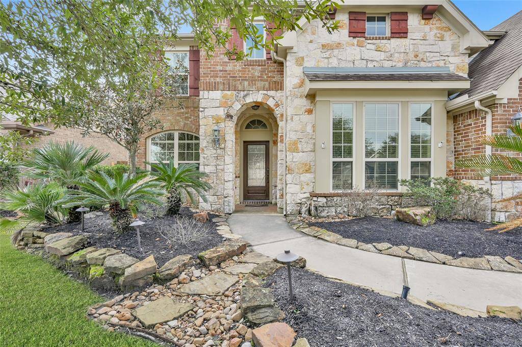 Exterior features a brick and stone front with an arched entry leading to the front porch. Architectural details include cedar shutters and corbels. Stacked stone lines the flower beds and sidewalk to the front door.