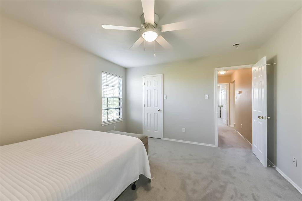 This upstairs bedroom features plush carpeting, a ceiling fan, and easy access to the hallway and nearby bathroom—ideal for guests or growing kids.