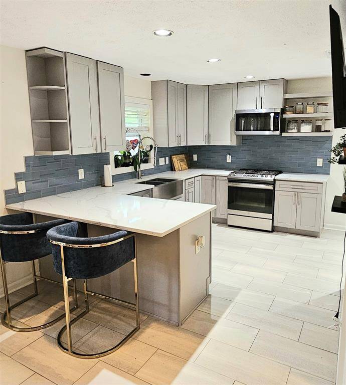 Beautifully remodeled kitchen featuring everything you could want or need—stunning fresh paint, sleek quartz countertops, and custom wooden shelving that offers plenty of stylish storage