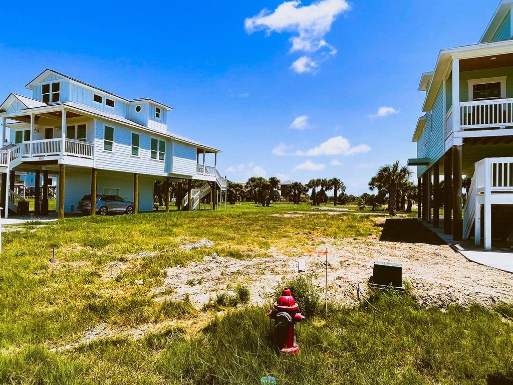 Elevated coastal homes on stilts with spacious yards, surrounded by lush greenery and palm trees under a clear blue sky.