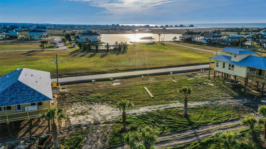 This photo showcases a serene coastal neighborhood with elevated homes and lush greenery. There's a road running through the area, and the view overlooks a picturesque body of water reflecting the sunset. Ideal for those seeking a tranquil, waterfront lifestyle.