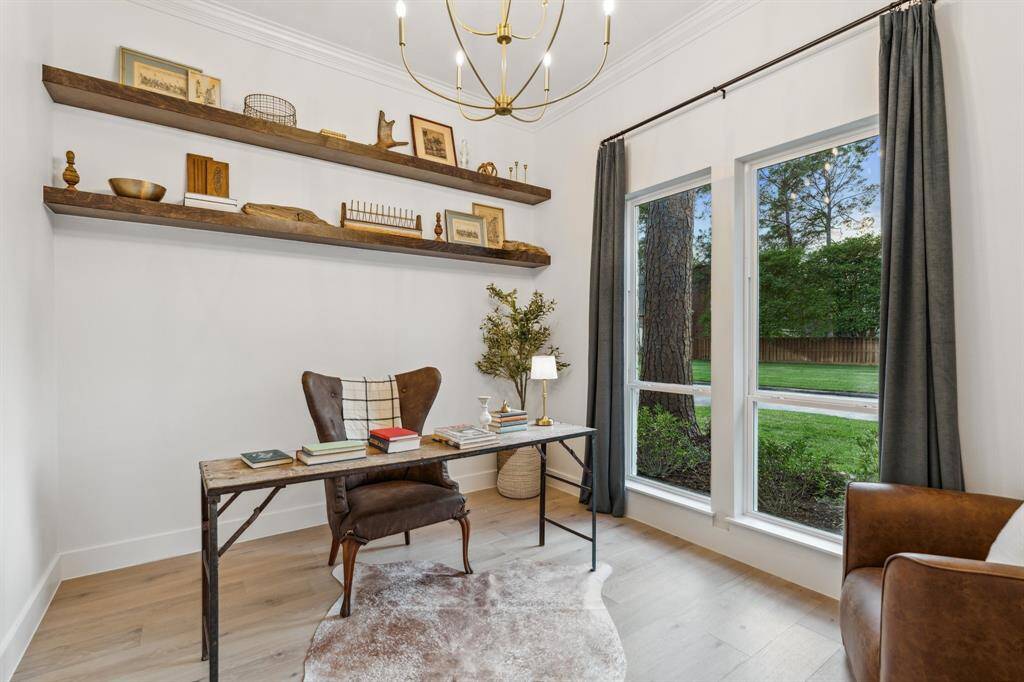 Working from home is a breeze in this functional and beautiful home office with floating shelves, large window, french doors, and chandelier.