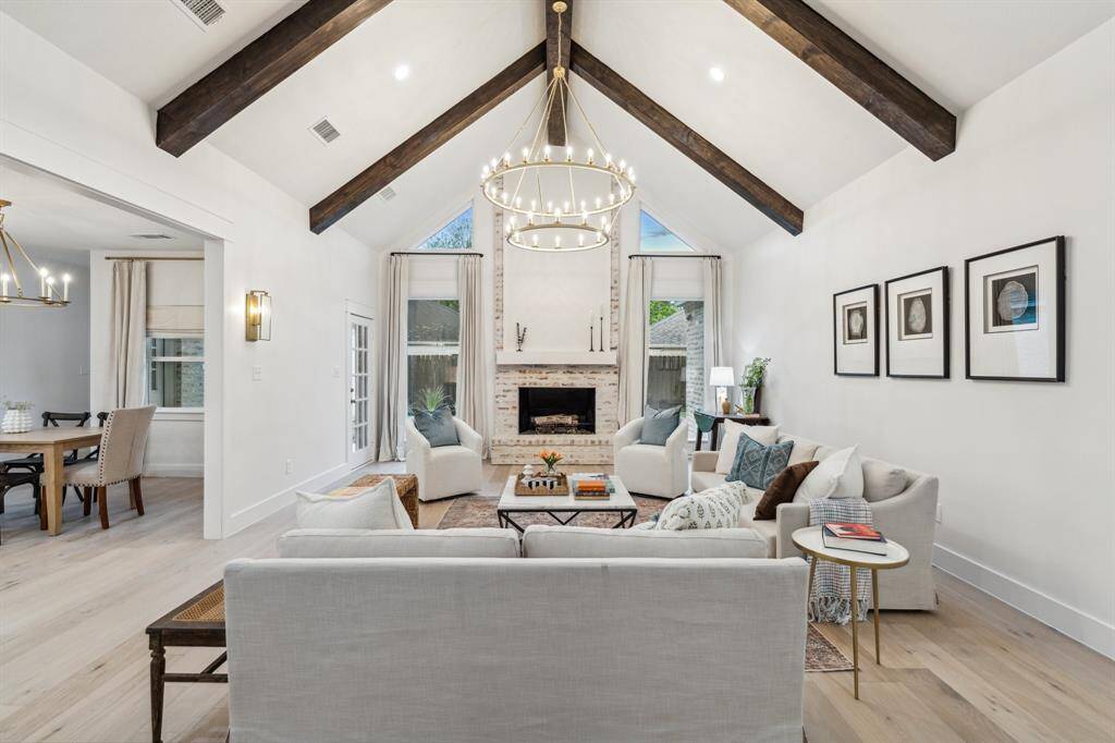 This living room features cathedral ceilings with wood beams, a stunning floor to ceiling fireplace, sconce lighting, and is open to the kitchen and breakfast room.