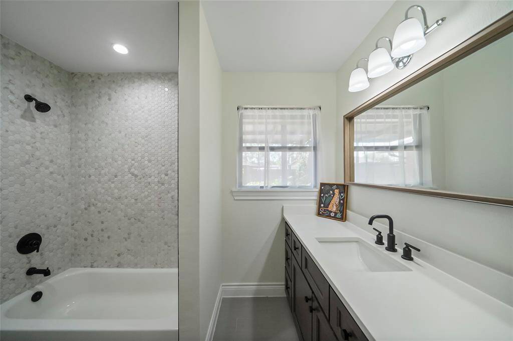 Here’s the spacious secondary bathroom, complete with a tub-shower combo, quartz countertops, and elegant floor-to-ceiling tilework.