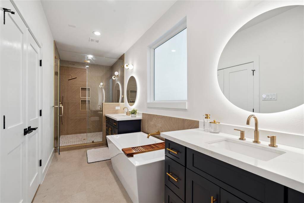 The primary ensuite is designed from inspiration for a resort style feel with separate sinks and champagne accents with a stunning set off backlit round mirrors with color tone options.