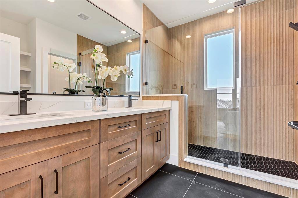Elegant main bathroom featuring a glass-enclosed shower, dual sinks, and a large vanity mirror. Plus, plenty of cabinet storage for all your essentials.