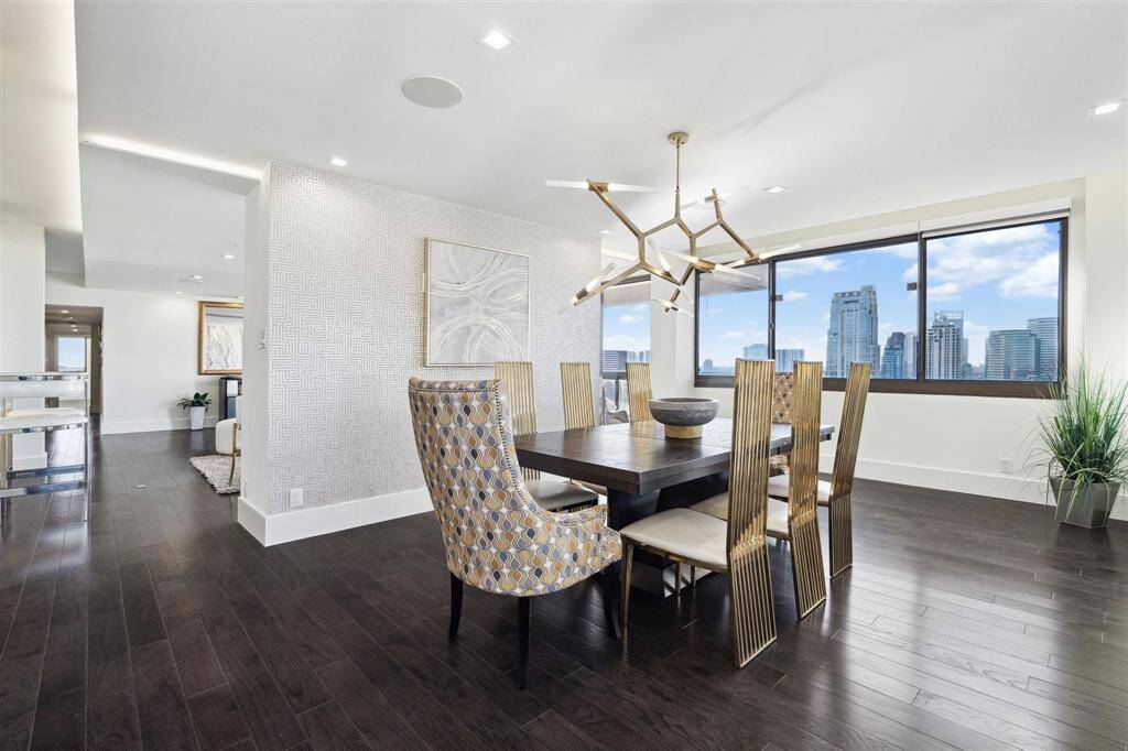 The spacious dining room showcases a wallpaper accent wall, updated chandelier, engineered hardwood floors, a drop tray ceiling with LED lighting, modern recessed lights, and a hardwired surround sound system.