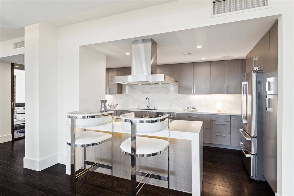 Another angle of the impressive kitchen showcasing a breakfast bar with seating for three. Ambient lighting under the cabinets and countertop, modern recessed lighting, hardwired surround sound speakers, and soft-close drawers and cabinets complete the space.