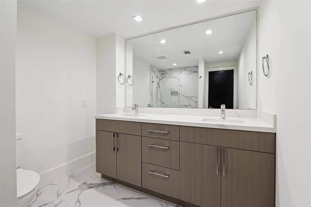 Spacious hallway bathroom featuring a large tub/shower combo with frameless glass, double sink vanity with Calacatta quartz countertops, and modern cabinetry.