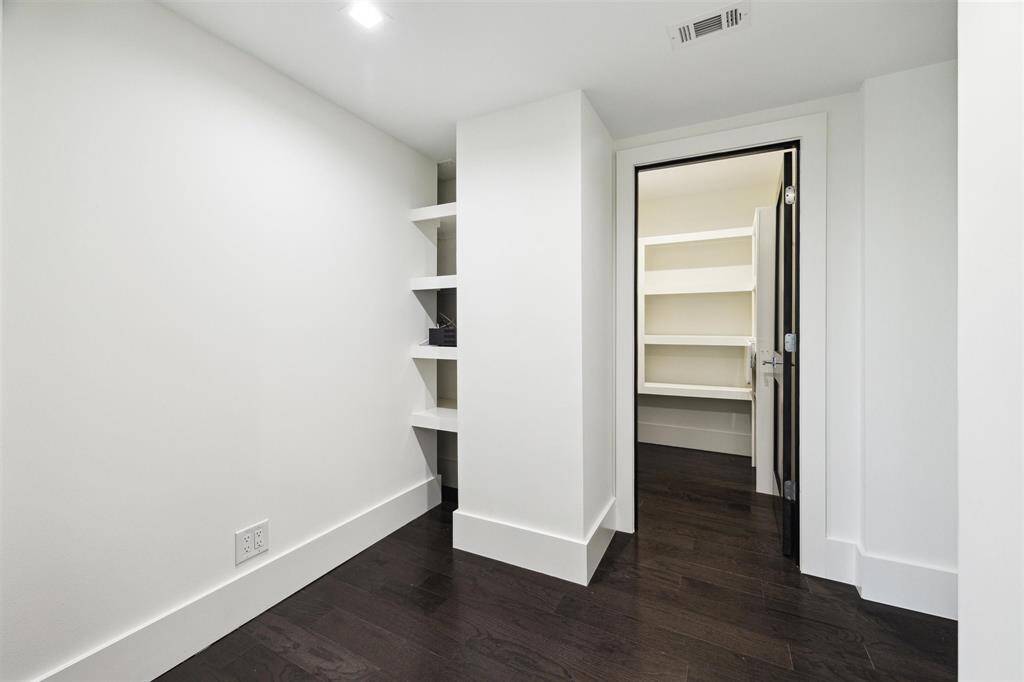 Versatile bonus room with built-in shelving, perfect for a home office, craft space, or wine cellar. Through the door is an additional storage closet with even more shelving for ample organization.