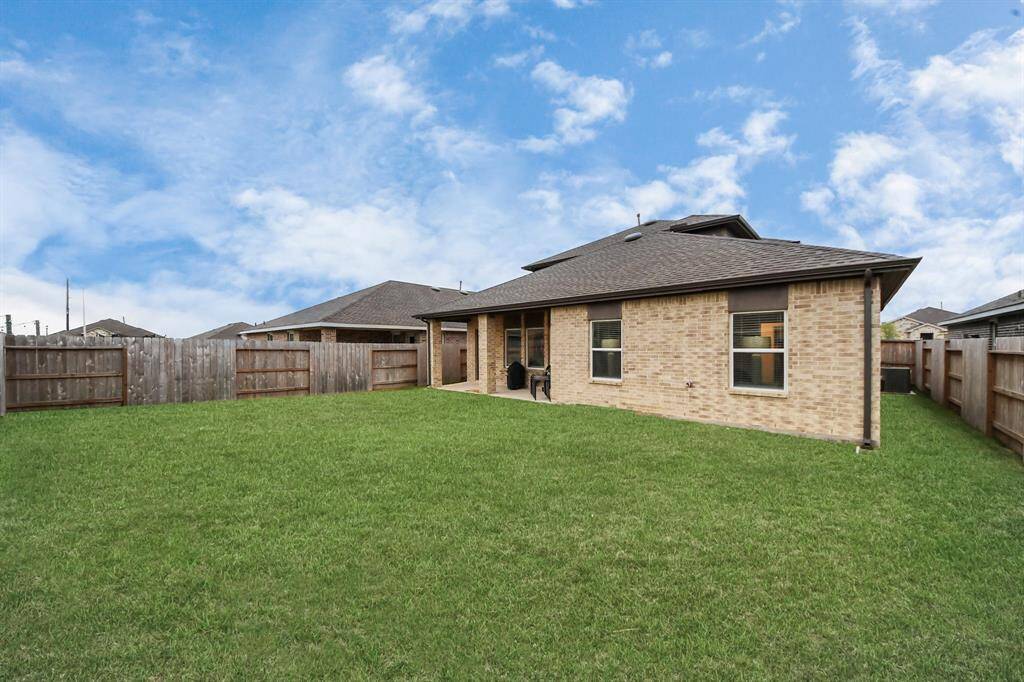 This photo shows a spacious backyard with a well-maintained lawn, bordered by a wooden fence. The house features a brick exterior and a covered patio, ideal for outdoor activities and relaxation.