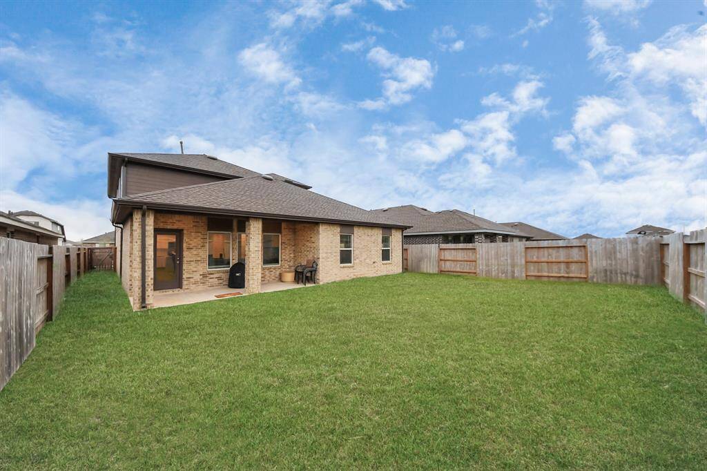 This photo showcases a spacious backyard with a lawn, bordered by a wooden fence. The brick house features a covered patio, ideal for outdoor activities and relaxation.