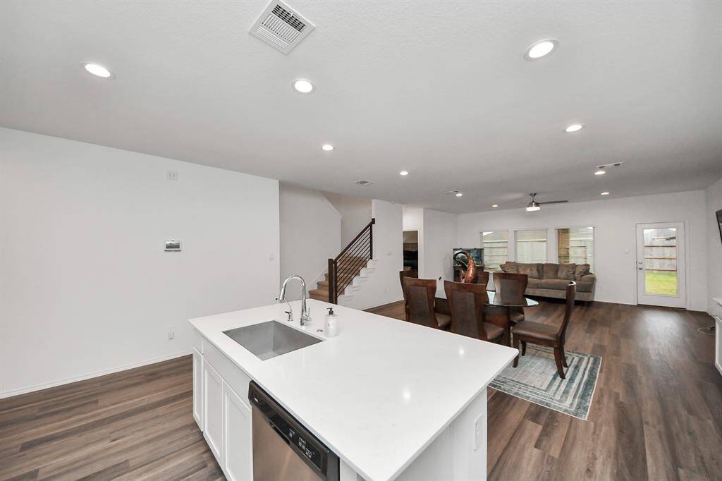 This open-concept living space features a modern kitchen with a central island, seamlessly connecting to a dining area and spacious living room. The room is well-lit with recessed lighting and has hardwood floors, creating a warm and inviting atmosphere. Large windows offer natural light and a view of the backyard.