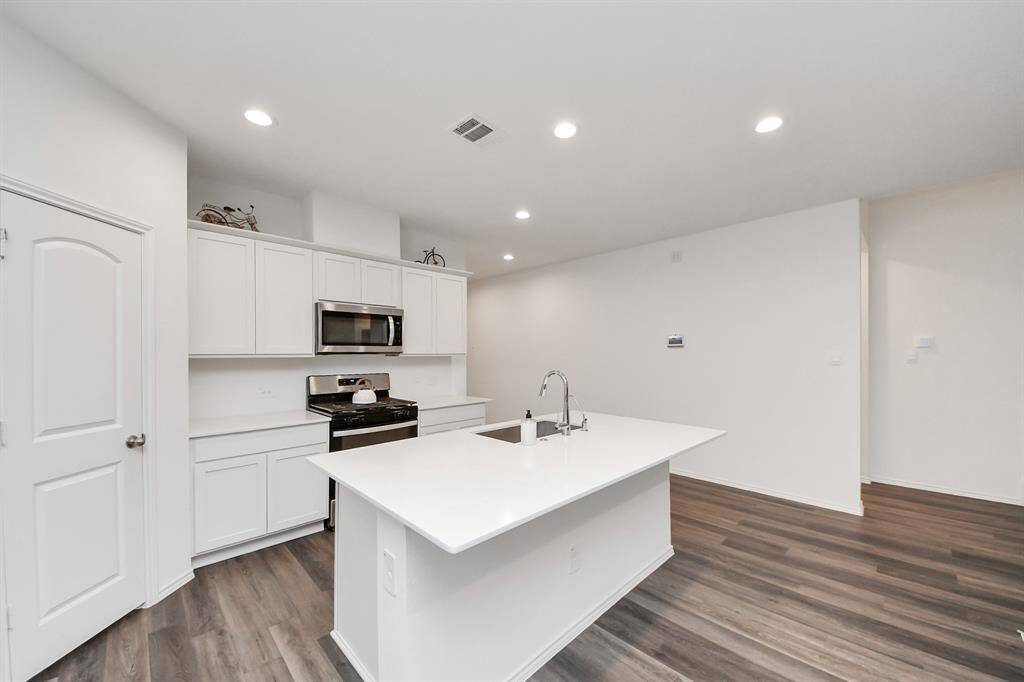 This modern kitchen features sleek white cabinetry, stainless steel appliances, and a spacious island with a sink. The open layout and recessed lighting create a bright and welcoming atmosphere, complemented by stylish wood flooring.