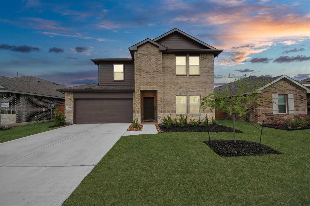This photo features a two-story brick home with a modern design. It has a two-car garage, a well-maintained front lawn, and minimal landscaping. The sky at sunset adds a warm backdrop to the property.