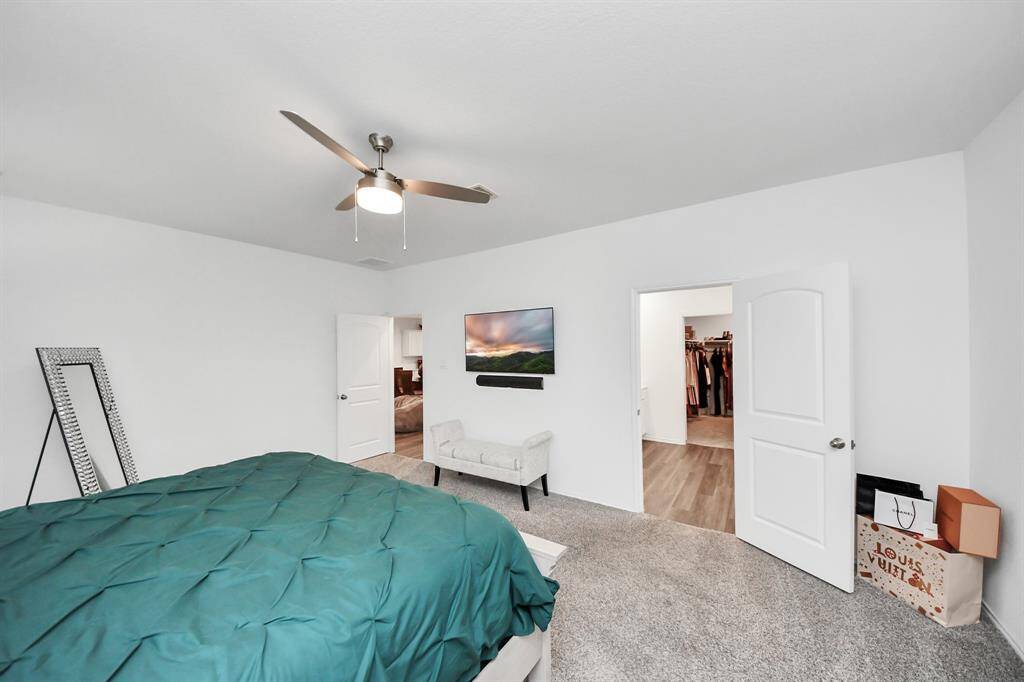Spacious primary bedroom featuring a modern ceiling fan, cozy carpet, and direct access to a generous primary en suite bath.