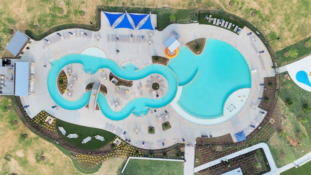 This aerial photo showcases a residential community with abundant amenities, including a large pool, playground, tennis courts, and green spaces. The area is surrounded by houses and has nearby water features, offering a family-friendly environment with recreational facilities.