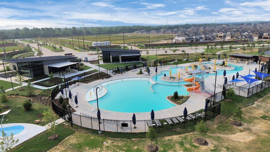 This photo showcases a modern community amenity center with a large, inviting pool featuring water slides and sunshades. The area is beautifully landscaped and includes a contemporary building, likely for events or gatherings. It's an attractive feature for potential homebuyers seeking a family-friendly neighborhood.