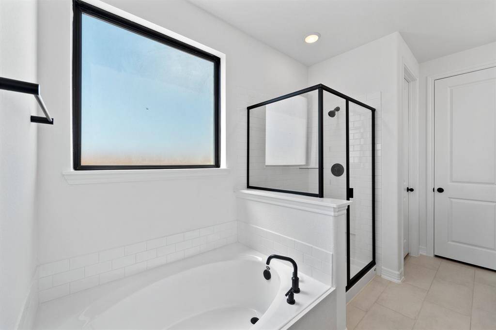 This additional view of your primary bathroom features tile flooring, fresh paint, walk-in shower, a separate garden tub, and a large walk-in closet.