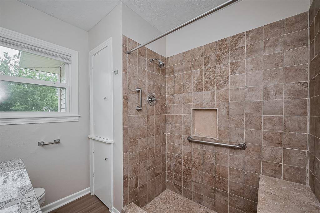 This full bathroom features a crisp vanity with under-sink storage, stylish lighting, and a large mirror. A window brings in soft daylight, while the shower area showcases lovely tilework.