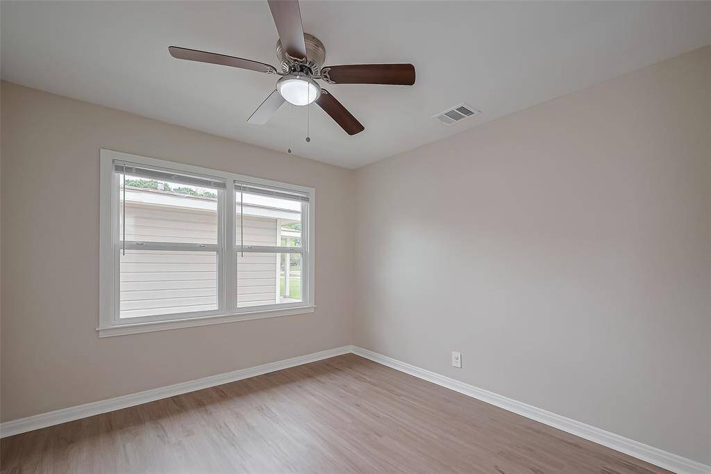 This bedroom continues the home’s cohesive style with smooth vinyl plank flooring, a broad window, and a ceiling fan. It’s a versatile space suited for rest, work, or play.