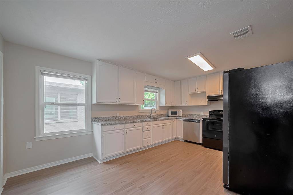 The kitchen is both bright and functional, featuring abundant white cabinetry above and below for effortless organization. The windows and warm linear lighting keep the space well-lit and welcoming, perfect for everyday meals or entertaining.