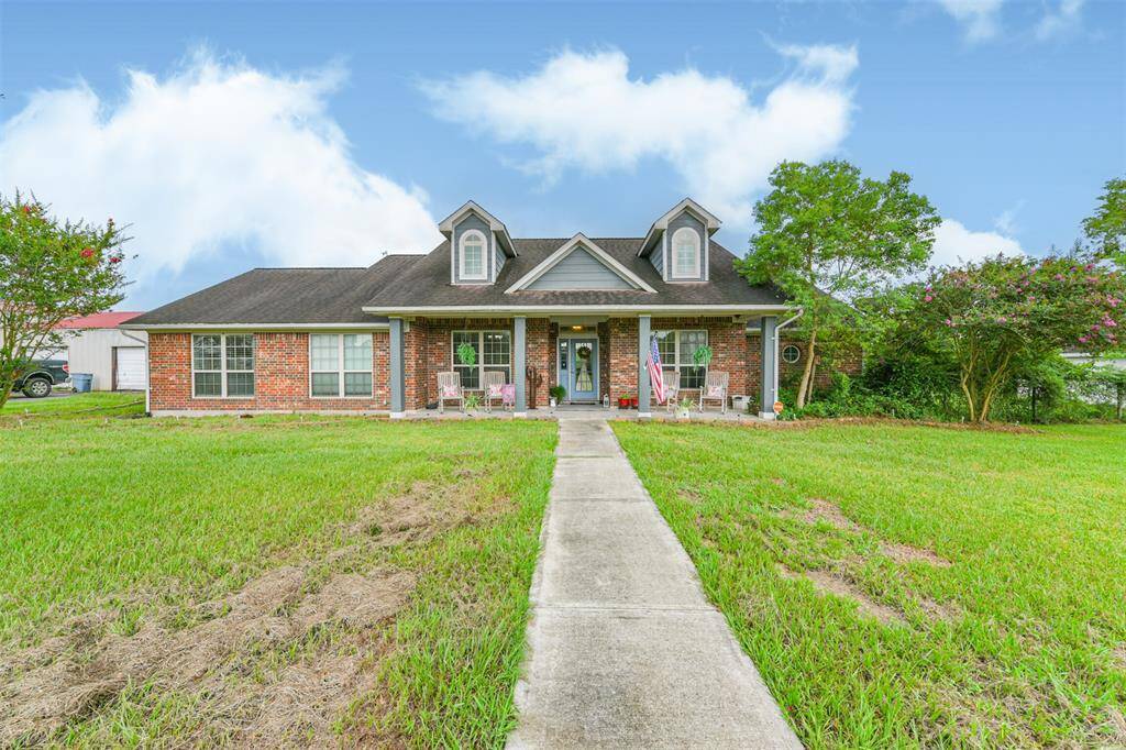 Charming single-story brick home featuring a de-attached garage, gabled roof, and a welcoming front porch, set on a lush green lawn with mature trees.