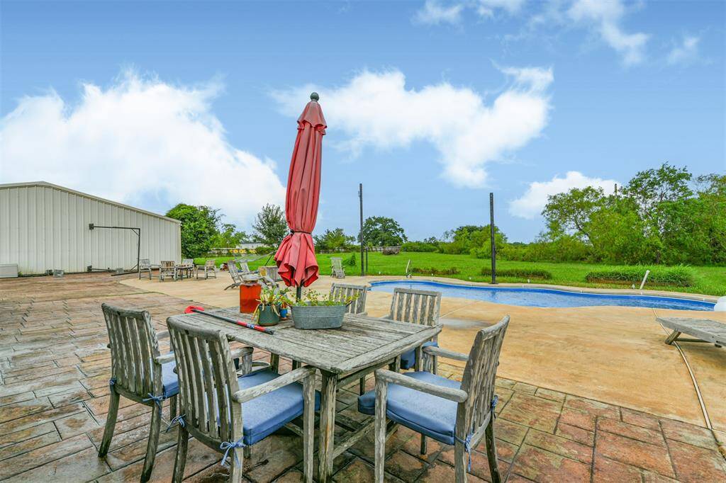 Spacious outdoor area featuring a large patio with dining set and umbrella, overlooking a private pool and expansive backyard. Ideal for entertaining and relaxation.