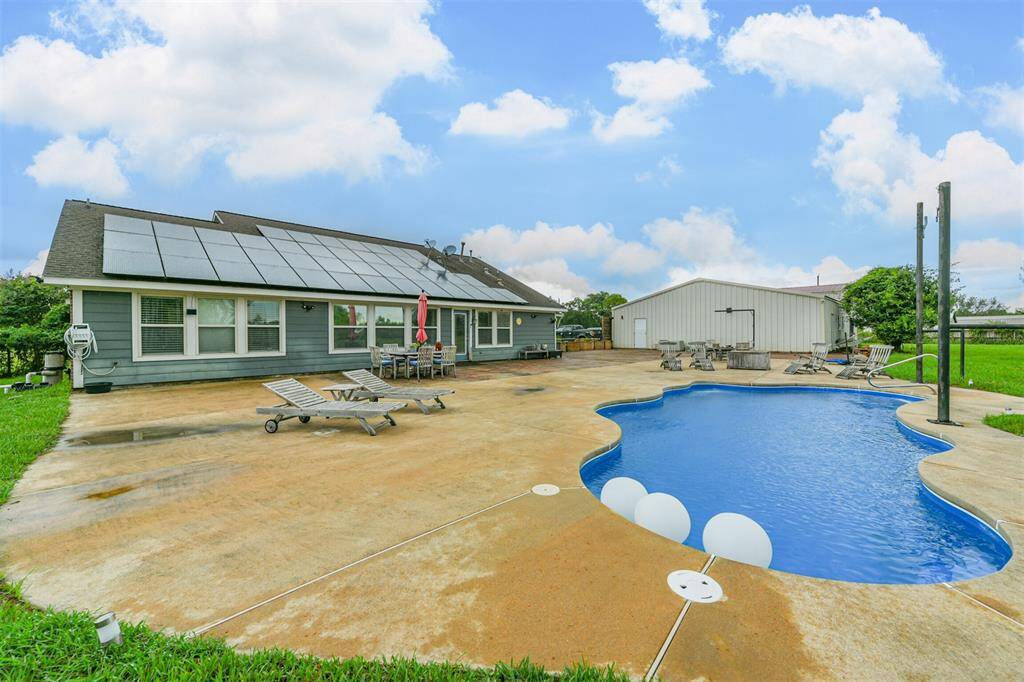 This is a single-story home with 47 solar panels on the roof, featuring a spacious backyard with an in-ground pool and a large outbuilding for storage or workshop space.