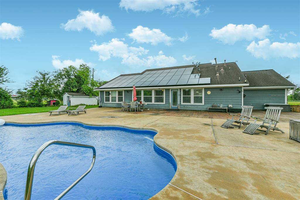 A single-story home with a solar panel roof and an in-ground pool, featuring a spacious patio area and a backyard.