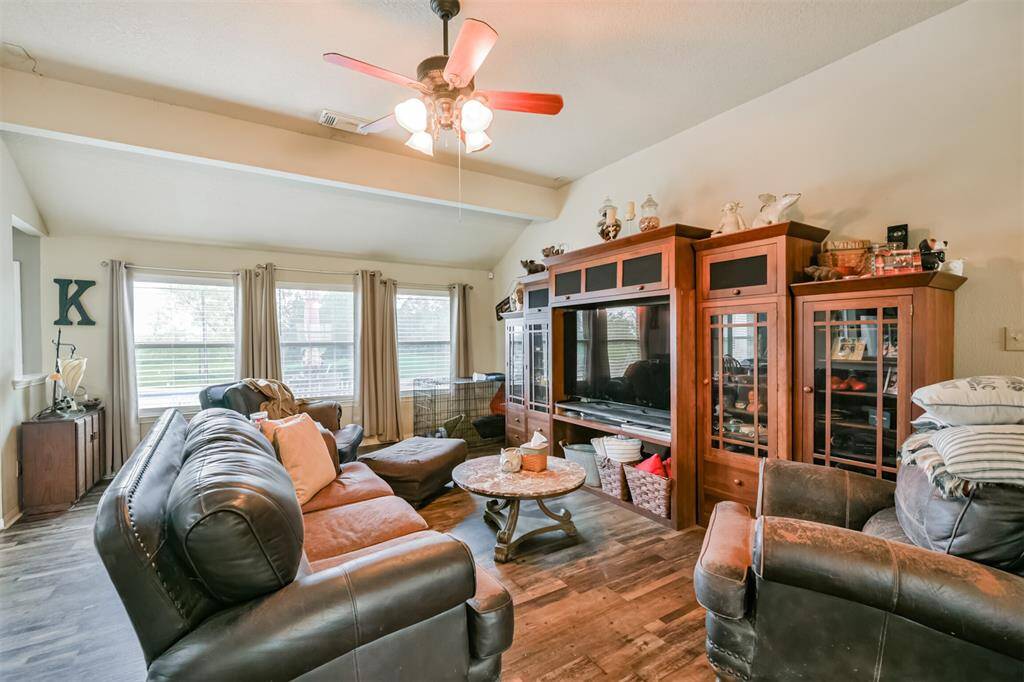 This is a cozy, well-lit living space featuring a large open area with a ceiling fan. Natural light streams in from multiple windows. The room is finished with neutral-toned walls and decorative touches that provide a homely atmosphere.