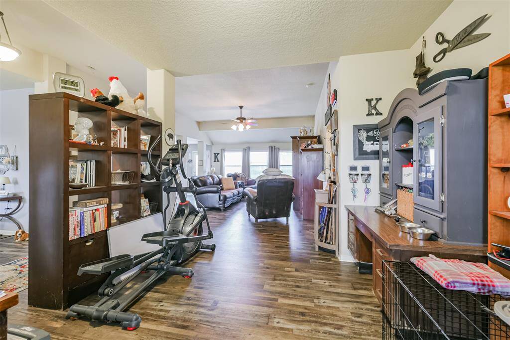 This is a well-lit, open-concept living space with hardwood floors, featuring a comfortable seating area, a bookshelf, and room for exercise equipment. Decorative elements add a personal touch to the space.