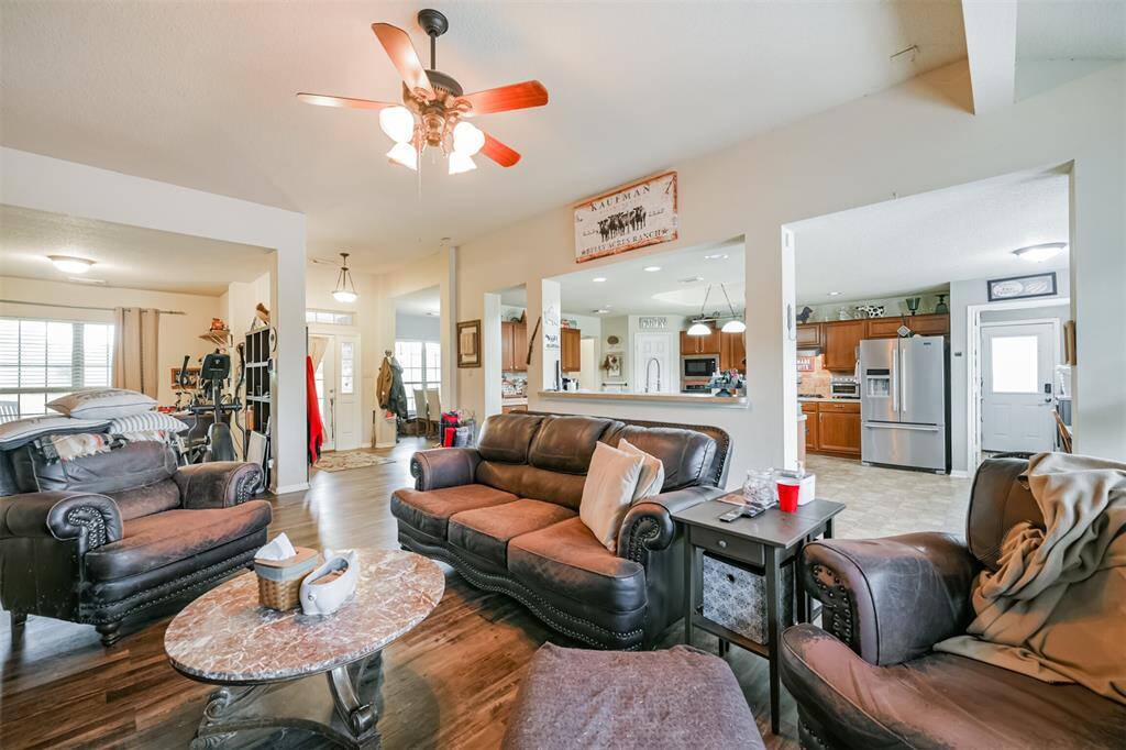 This is an open-concept living space with a cohesive flow into the kitchen area. It features hardwood flooring, ample natural light, and a warm, inviting color palette. The kitchen is equipped with modern stainless-steel appliances and an abundance of cabinet space.