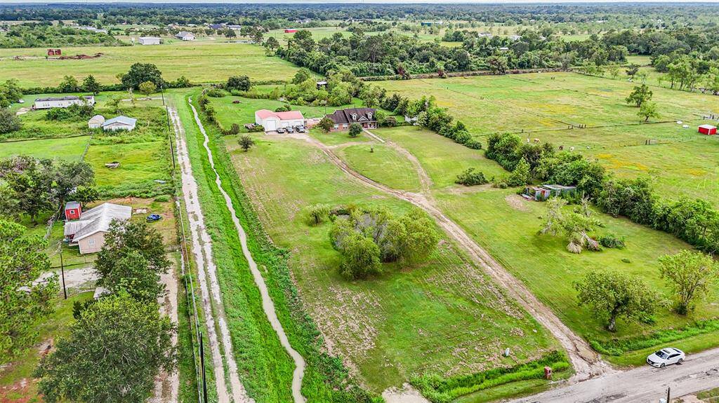 Aerial view of a spacious rural property with green fields, and surrounding trees, offering a peaceful, country living atmosphere.