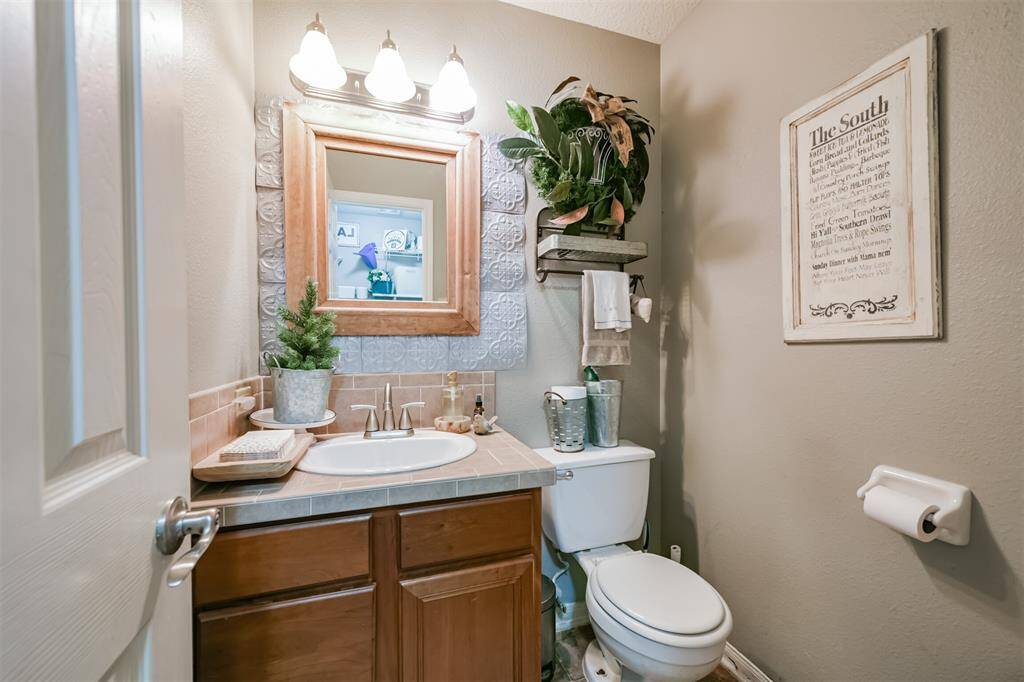 This is a cozy and well-maintained half-bathroom featuring a single vanity with storage below, a framed mirror with overhead lighting, a toilet, and decorative shelving.