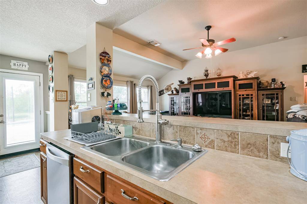 This is a spacious and well-lit kitchen featuring ample counter space with a dual basin sink, modern appliances, and an open layout that flows into the living area. There is a glass door leading outside, providing plenty of natural light and easy access to outdoor spaces.